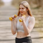 Fit woman lifting dumbbells on a sunny day, embracing a healthy outdoor workout.